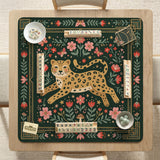Dark green square mahjong mat with a golden spotted leopard in the center, surrounded by flowers, leafy stems, butterflies, and small star accents.