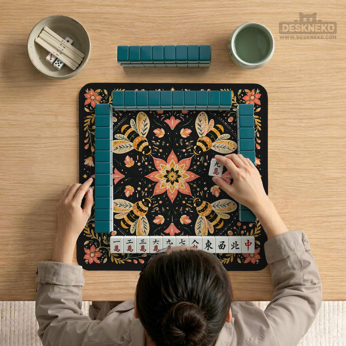 Black mahjong mat with a symmetrical botanical design, coral flowers, golden leaves, and small bees.