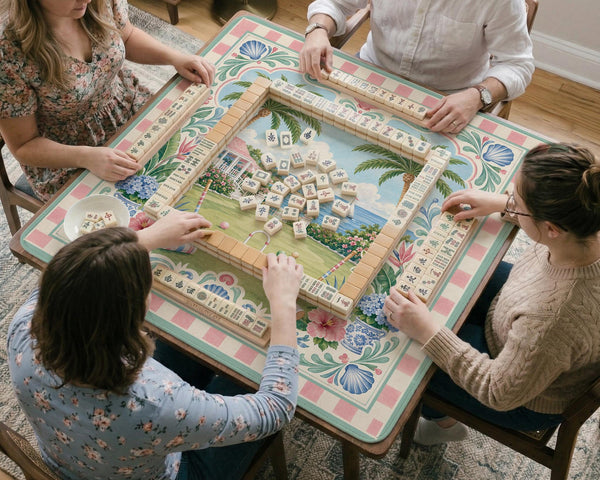 Pastel mahjong mat with a pink gingham border, seashells, hydrangea pots, palm trees, croquet details, and a coastal garden scene.