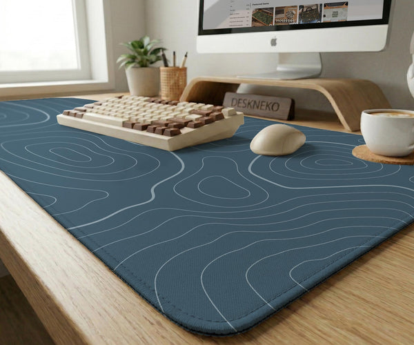 A slate blue desk mat with thin contour line map art on a light background.