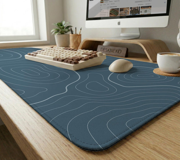 A slate blue desk mat with thin contour line map art on a light background.