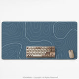 A slate blue desk mat with thin contour line map art on a light background.