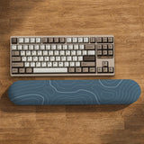 Muted blue desk mat with thin topographic line art pattern shown with matching mousepad and keyboard wrist rest options.