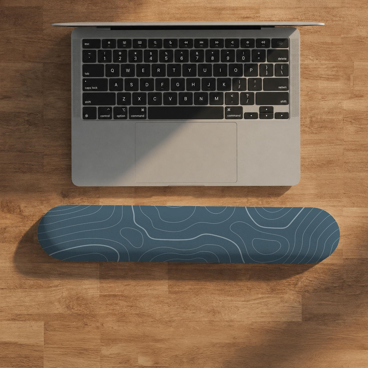 Muted blue desk mat with thin topographic line art pattern shown with matching mousepad and keyboard wrist rest options.
