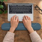 Muted blue desk mat with thin topographic line art pattern shown with matching mousepad and keyboard wrist rest options.