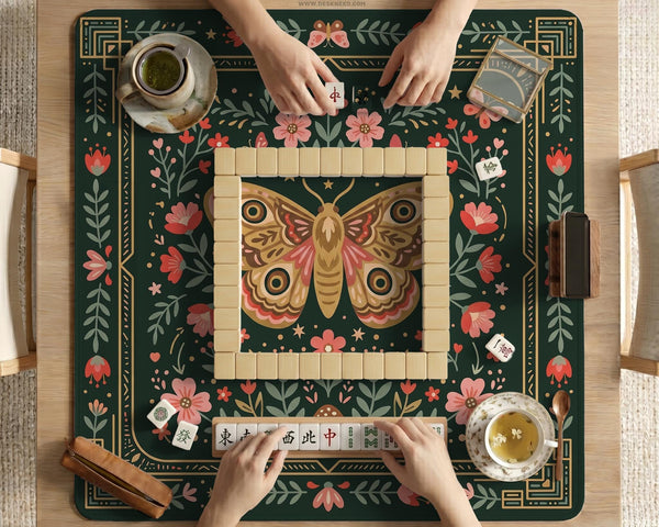Dark green square mahjong mat with floral branches, small red blossoms, gold line details, and a large moth in the center.