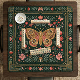 Dark green square mahjong mat with floral branches, small red blossoms, gold line details, and a large moth in the center.