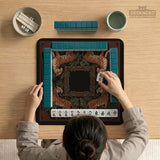Black square mahjong mat with mirrored tiger faces, bamboo, dark tropical leaves, ornate border details, and orange accents.
