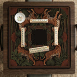 Black square mahjong mat with mirrored tiger faces, bamboo, dark tropical leaves, ornate border details, and orange accents.