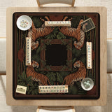 Black square mahjong mat with mirrored tiger faces, bamboo, dark tropical leaves, ornate border details, and orange accents.