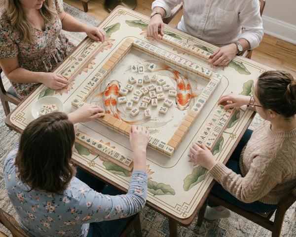 Ivory square mahjong mat with watercolor koi fish, lotus flowers, peach blossoms, sage leaves, and a thin gold border.