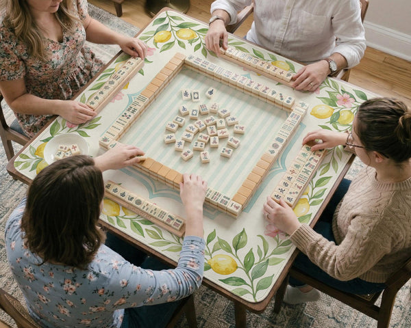 Square yellow mahjong mat with a citrus garden border, green vines, pink blossoms, aqua accents, and a plain center play area.