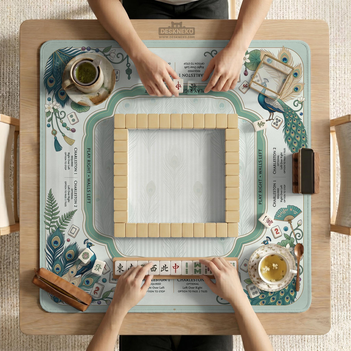 Teal square mahjong mat with peacock feathers, soft floral pattern, tassel details, and printed rule guide text in the center.