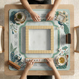 Teal square mahjong mat with peacock feathers, soft floral pattern, tassel details, and printed rule guide text in the center.