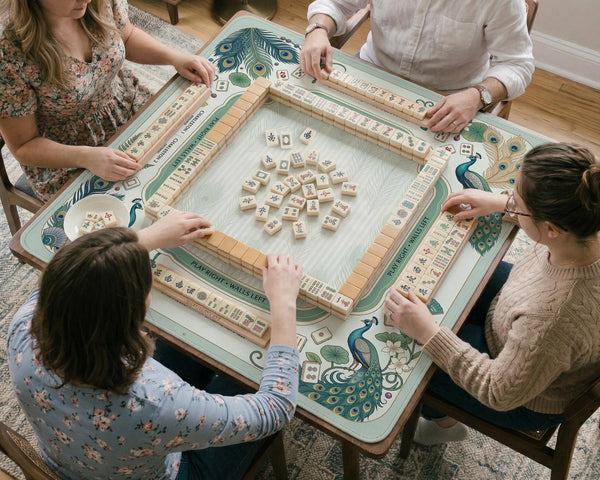 Teal square mahjong mat with peacock feathers, soft floral pattern, tassel details, and printed rule guide text in the center.