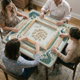 Teal square mahjong mat with peacock feathers, soft floral pattern, tassel details, and printed rule guide text in the center.