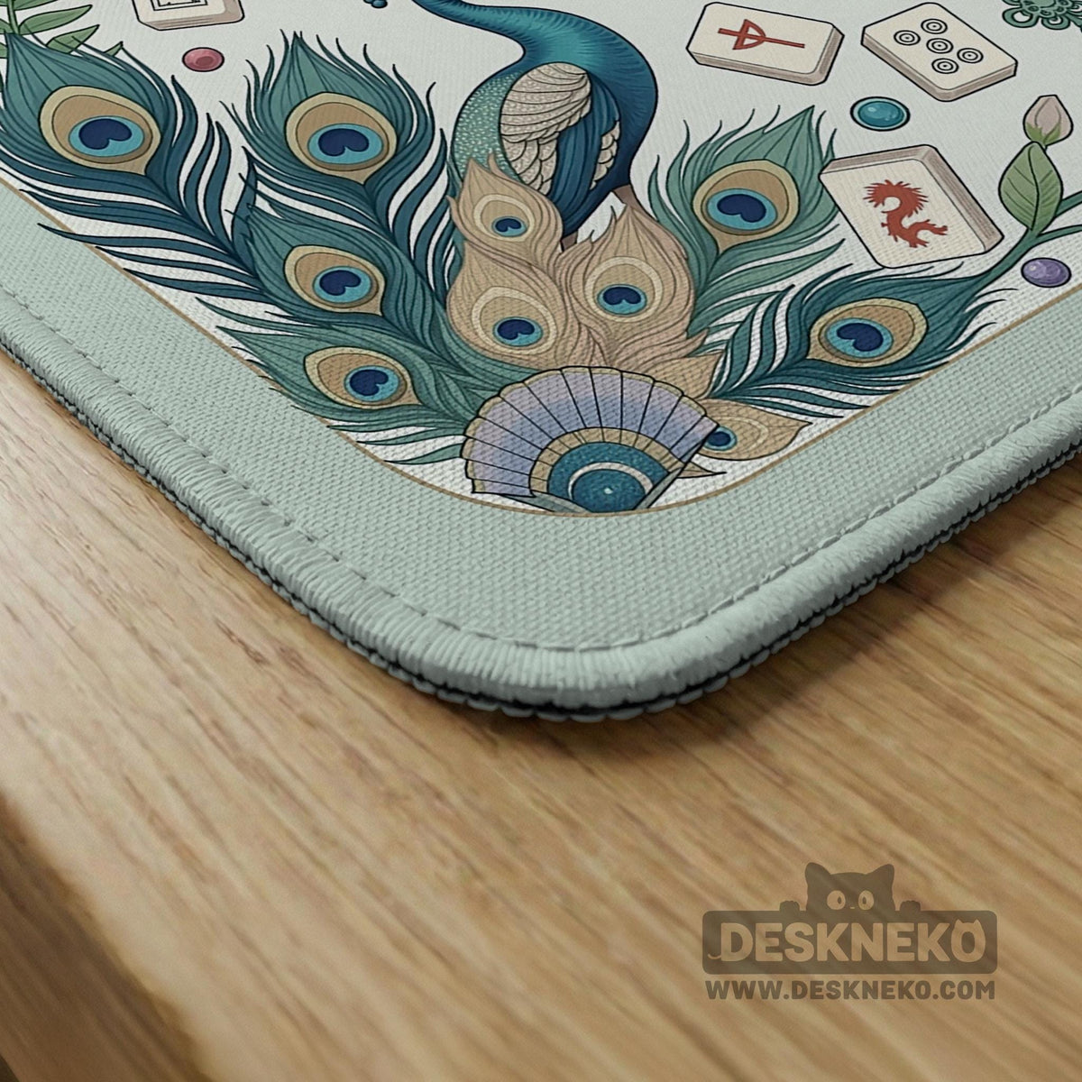 Teal square mahjong mat with peacock feathers, soft floral pattern, tassel details, and printed rule guide text in the center.