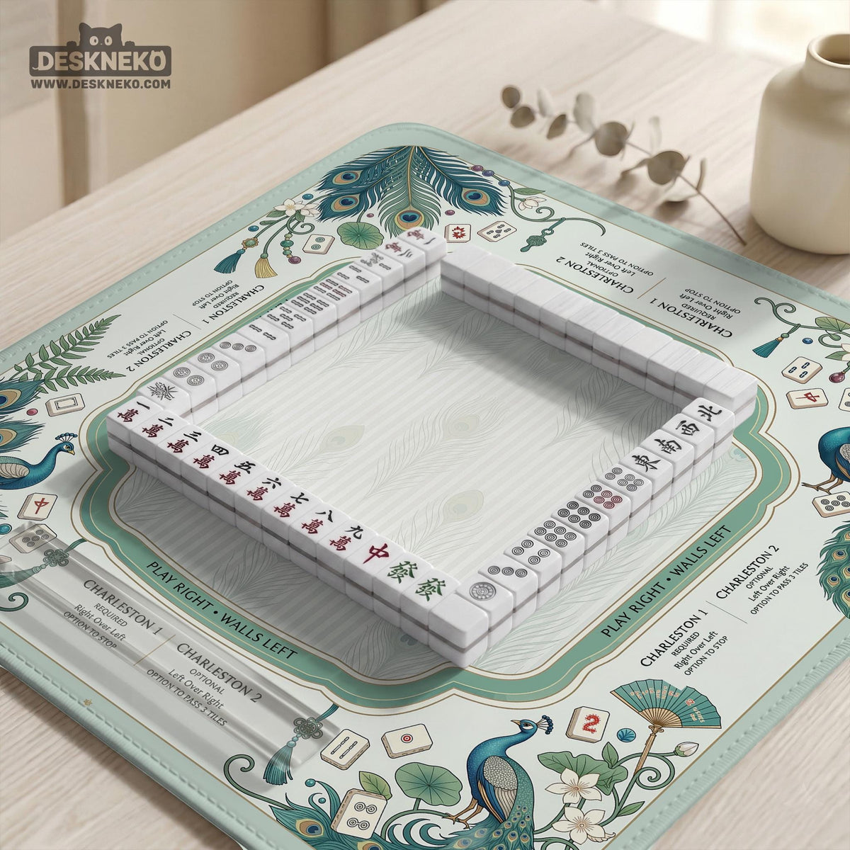 Teal square mahjong mat with peacock feathers, soft floral pattern, tassel details, and printed rule guide text in the center.