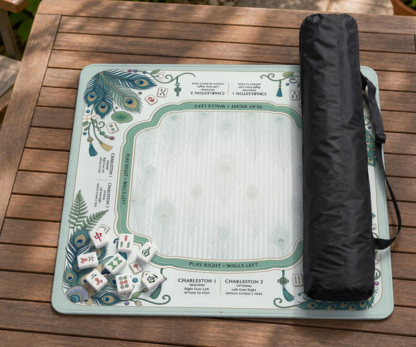 Teal square mahjong mat with peacock feathers, soft floral pattern, tassel details, and printed rule guide text in the center.