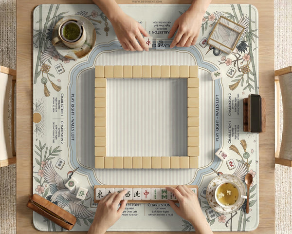 Beige square mahjong mat with a sage border, crane birds, bamboo, flowers, tile icons, and printed rules around a clean center play area.
