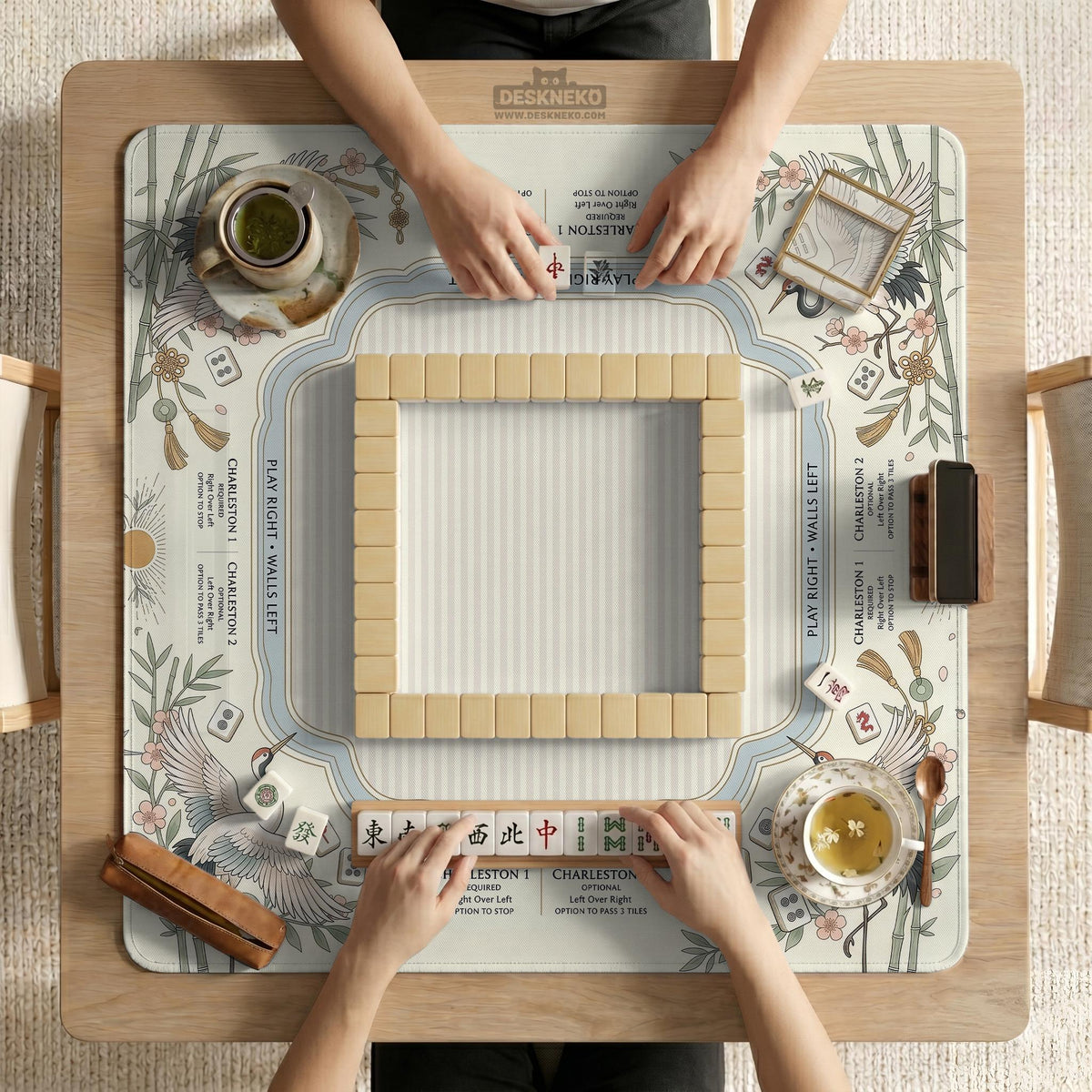 Beige square mahjong mat with a sage border, crane birds, bamboo, flowers, tile icons, and printed rules around a clean center play area.