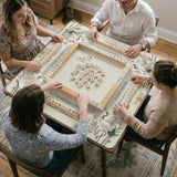 Beige square mahjong mat with a sage border, crane birds, bamboo, flowers, tile icons, and printed rules around a clean center play area.