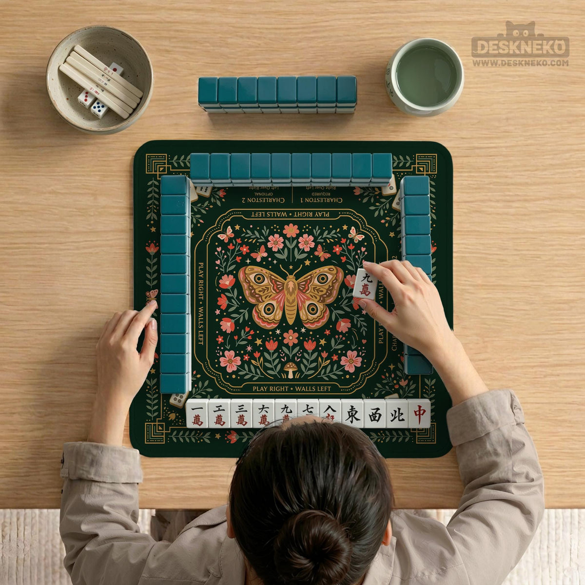 Dark botanical mahjong table mat with a floral border, large moth and butterfly design in the center, gold corner frame, and printed rules layout around the edge.