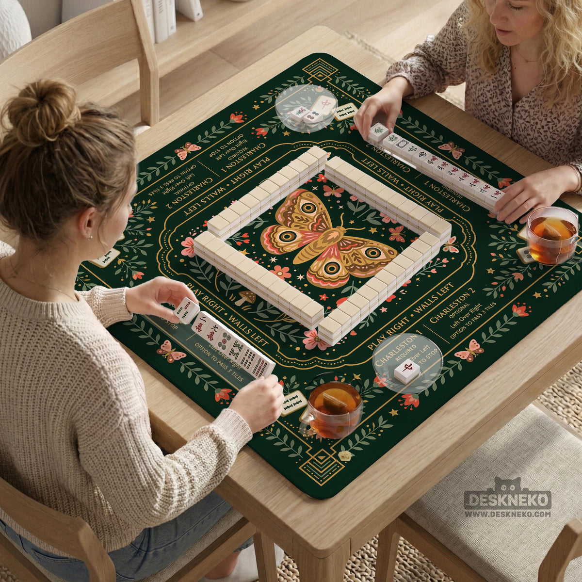Dark botanical mahjong table mat with a floral border, large moth and butterfly design in the center, gold corner frame, and printed rules layout around the edge.