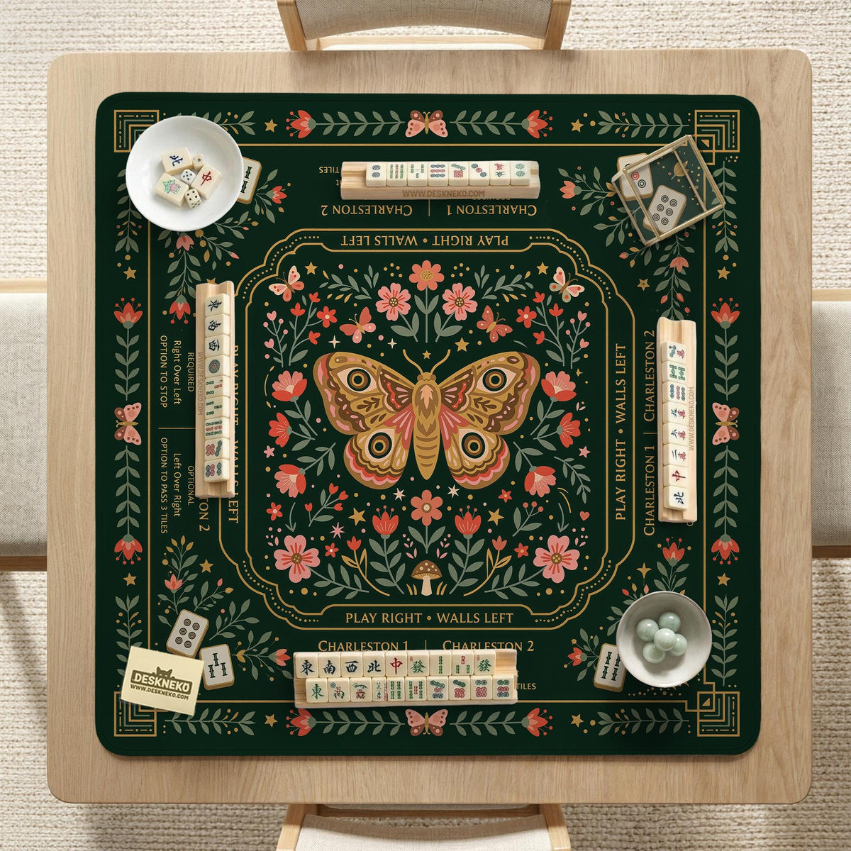 Dark botanical mahjong table mat with a floral border, large moth and butterfly design in the center, gold corner frame, and printed rules layout around the edge.
