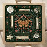 Dark botanical mahjong table mat with a floral border, large moth and butterfly design in the center, gold corner frame, and printed rules layout around the edge.