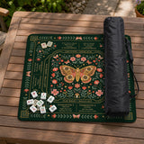 Dark botanical mahjong table mat with a floral border, large moth and butterfly design in the center, gold corner frame, and printed rules layout around the edge.