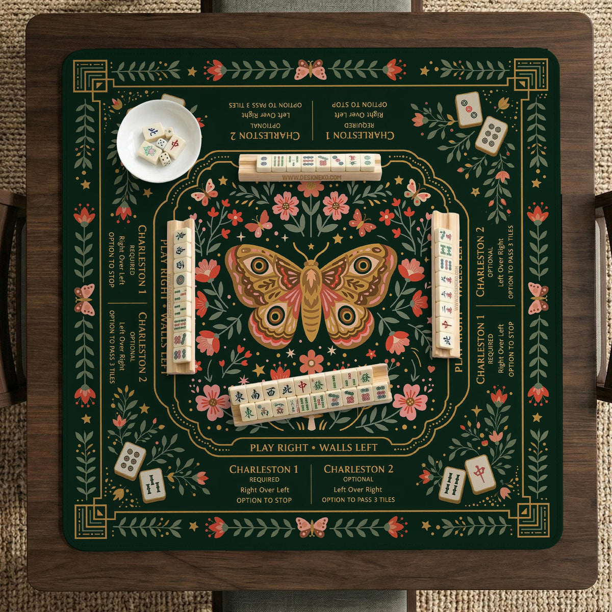 Dark botanical mahjong table mat with a floral border, large moth and butterfly design in the center, gold corner frame, and printed rules layout around the edge.