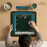 Square emerald green mahjong mat with bamboo line art, gold geometric cloud shapes, and a plain center playing area.