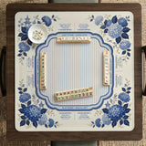 Blue and white mahjong table mat with a floral border, small birds, pagoda details, striped center, and printed rules around the edge.