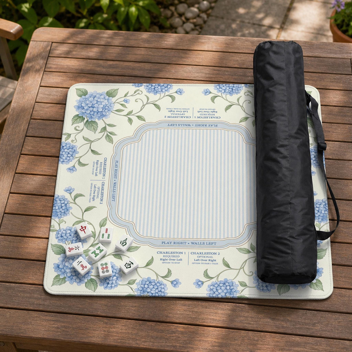 A square mahjong mat with blue hydrangea flowers, green vines, a cream background, a striped center, and printed rules around the border.