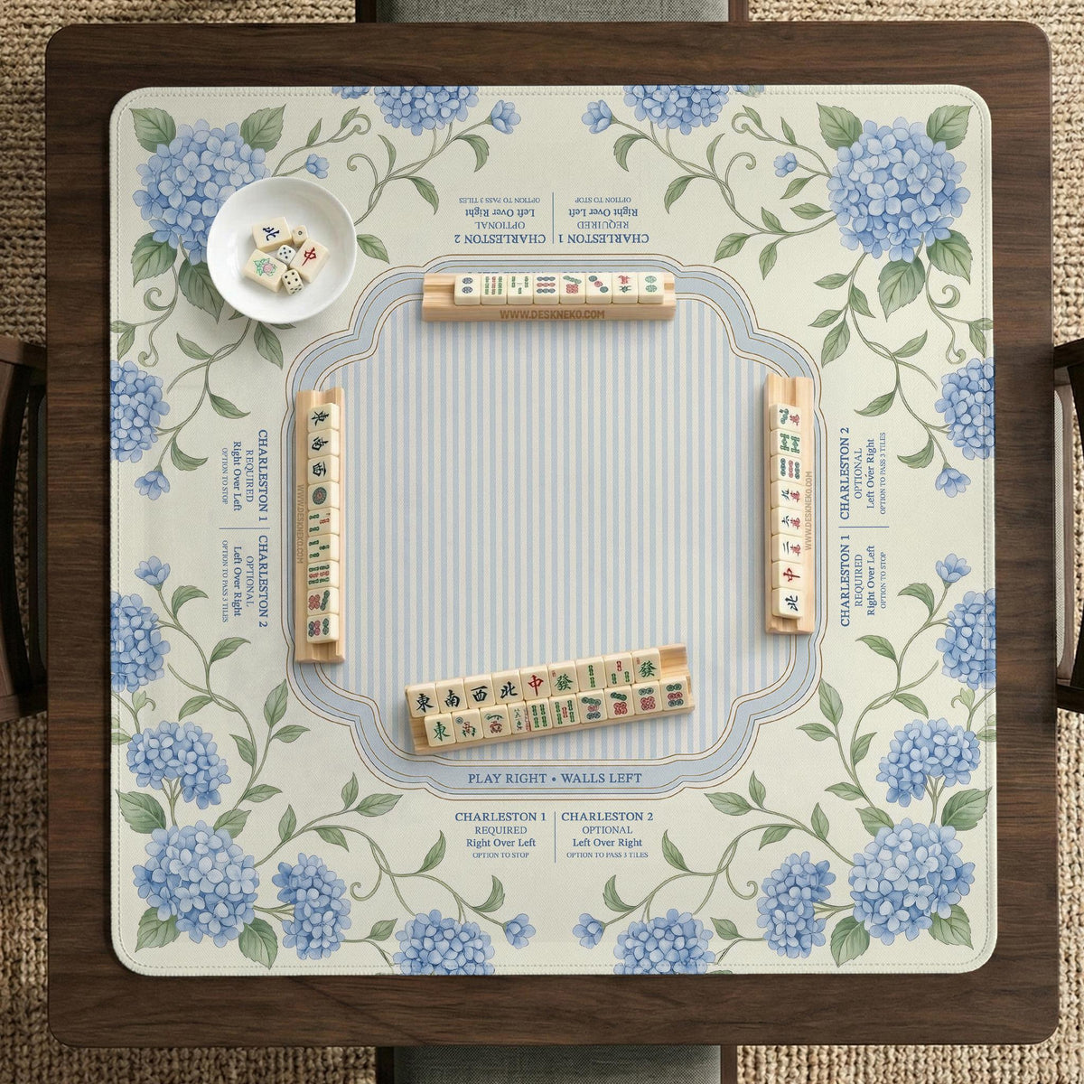 A square mahjong mat with blue hydrangea flowers, green vines, a cream background, a striped center, and printed rules around the border.