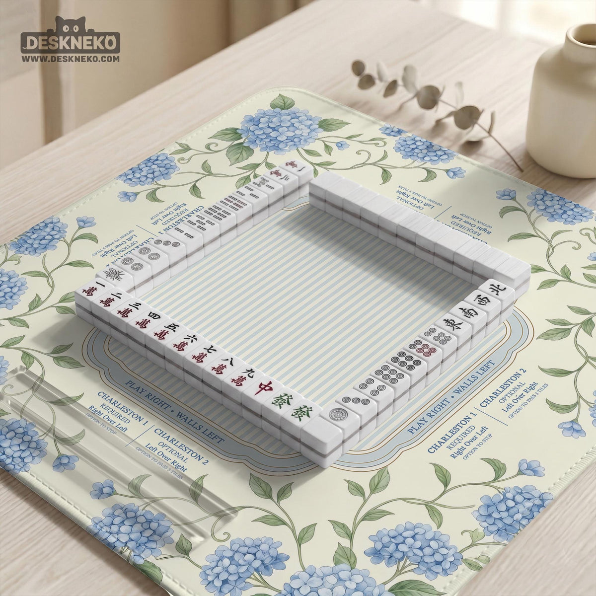 A square mahjong mat with blue hydrangea flowers, green vines, a cream background, a striped center, and printed rules around the border.