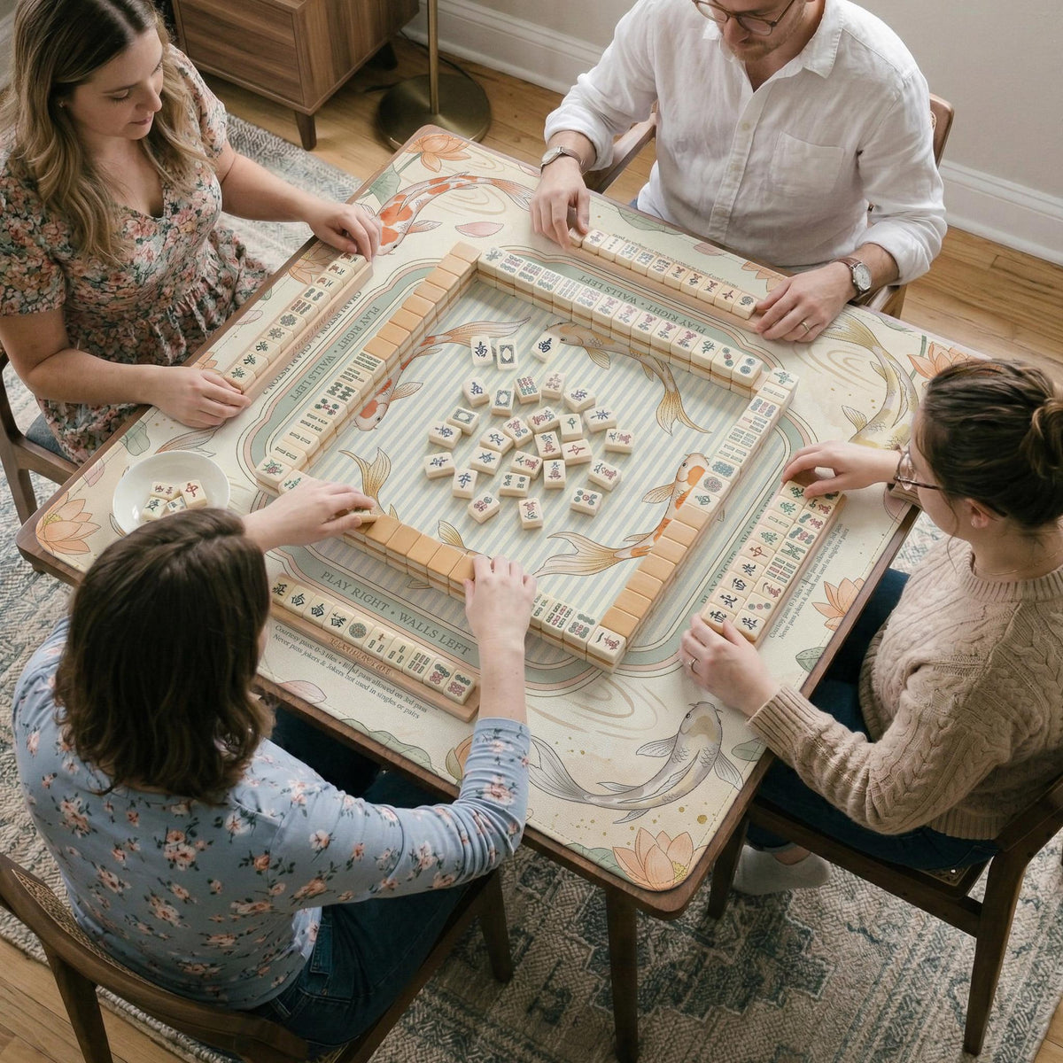 Sage and cream mahjong mat with a koi fish pond pattern, lotus blooms, water ripples, and printed instructions around the border. One version has a scalloped edge.
