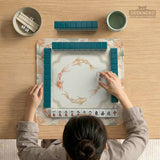 Sage and cream mahjong mat with a koi fish pond pattern, lotus blooms, water ripples, and printed instructions around the border. One version has a scalloped edge.
