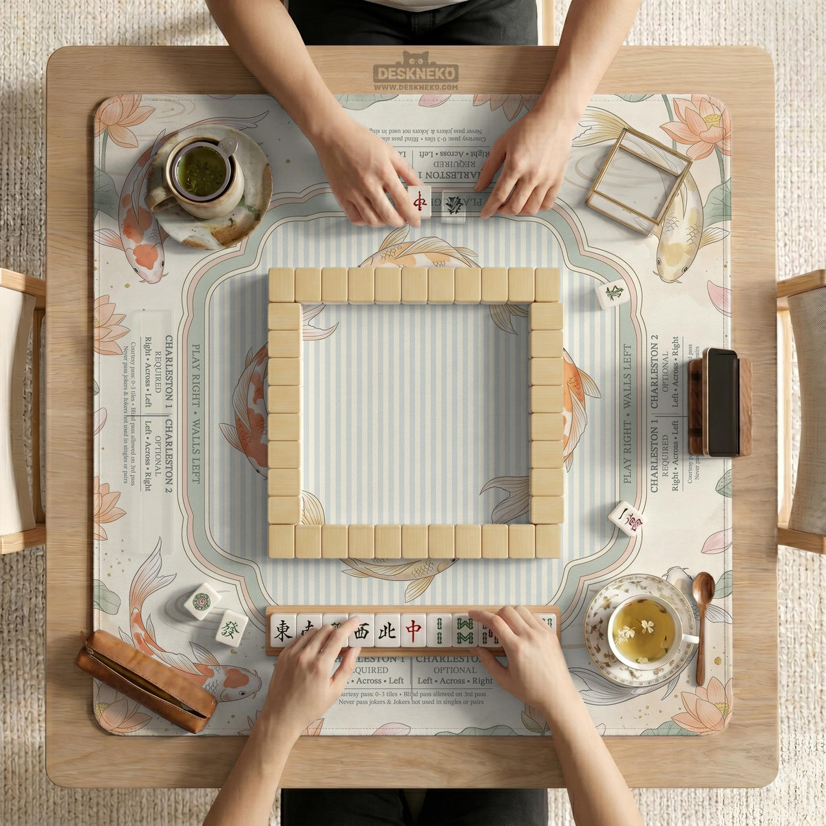 Sage and cream mahjong mat with a koi fish pond pattern, lotus blooms, water ripples, and printed instructions around the border. One version has a scalloped edge.