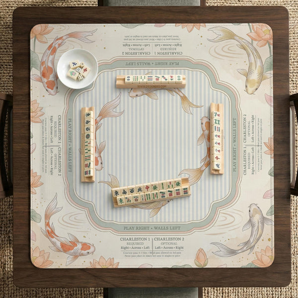 Sage and cream mahjong mat with a koi fish pond pattern, lotus blooms, water ripples, and printed instructions around the border. One version has a scalloped edge.