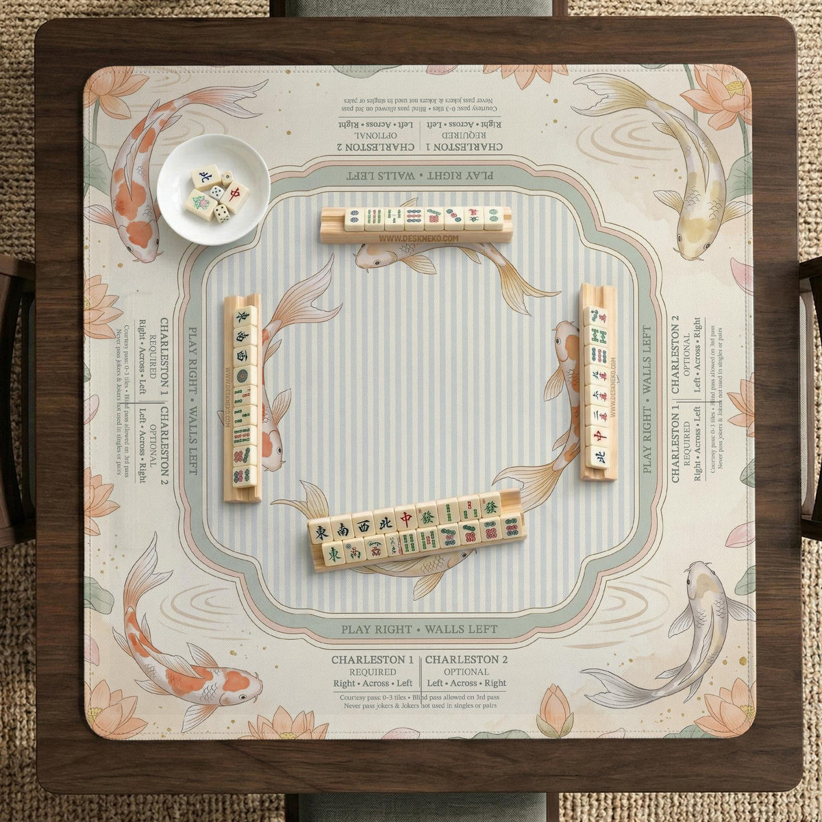 Sage and cream mahjong mat with a koi fish pond pattern, lotus blooms, water ripples, and printed instructions around the border. One version has a scalloped edge.