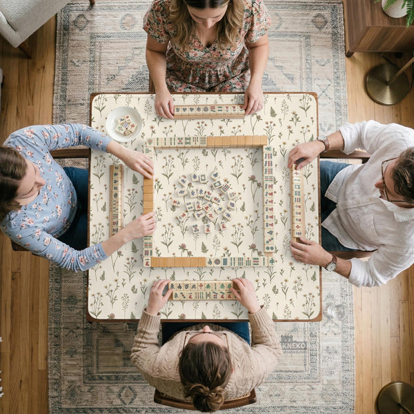 Cream mahjong mat with a floral pattern of small wildflowers and sage leaves, shown with a scalloped edge on a light neutral background.