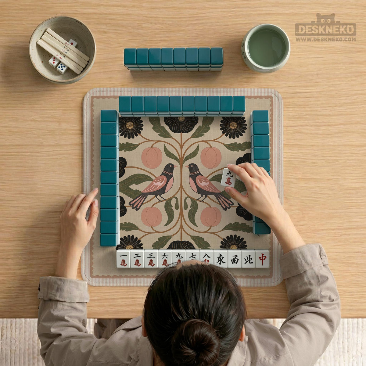 Beige mahjong mat with a botanical floral bird design, blush flowers, olive green leaves, black flower accents, and a warm linen-style background. Scalloped edge option shown.
