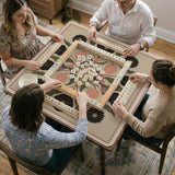Beige mahjong mat with a botanical floral bird design, blush flowers, olive green leaves, black flower accents, and a warm linen-style background. Scalloped edge option shown.