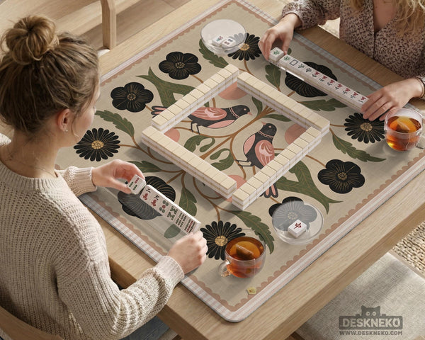 Beige mahjong mat with a botanical floral bird design, blush flowers, olive green leaves, black flower accents, and a warm linen-style background. Scalloped edge option shown.