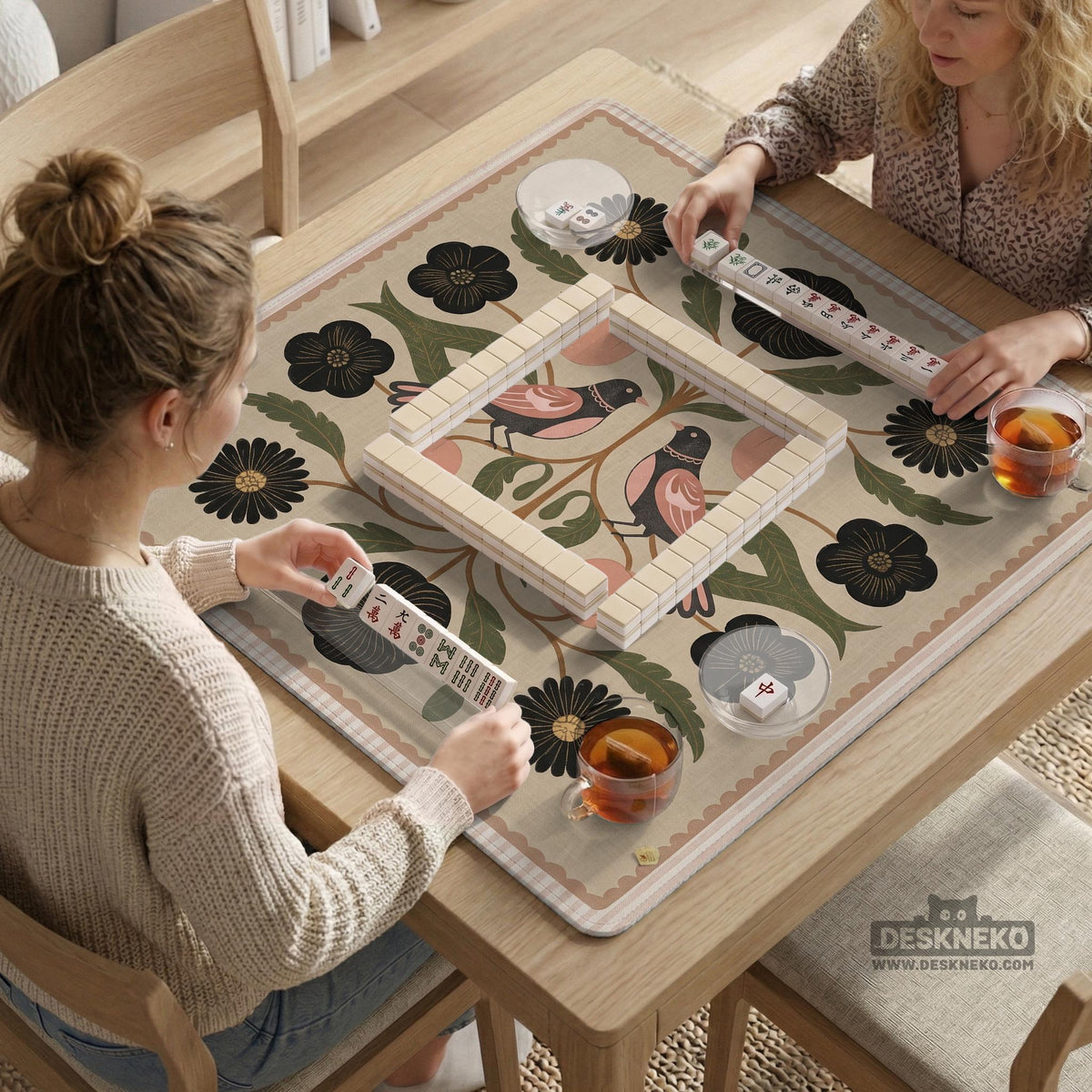 Beige mahjong mat with a botanical floral bird design, blush flowers, olive green leaves, black flower accents, and a warm linen-style background. Scalloped edge option shown.