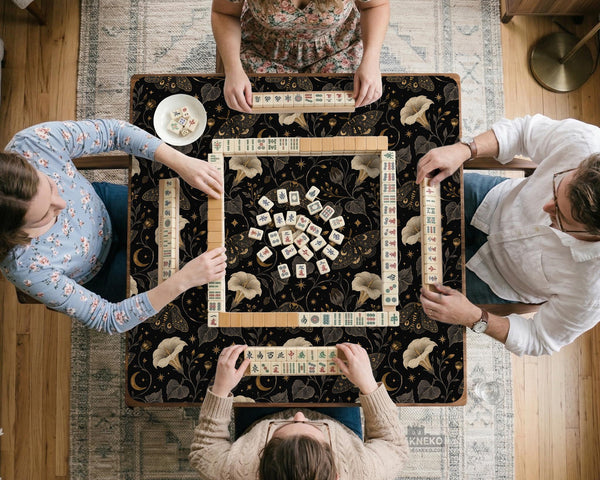 Black square mahjong mat with moths, moonflowers, crescent moons, and scattered stars in a celestial floral pattern.