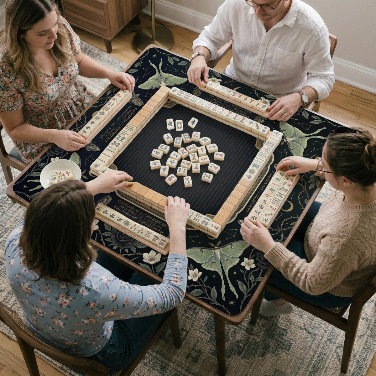 A dark floral mahjong mat with a scalloped edge, moth and flower artwork, and an American Mahjong rules layout on a dark background.