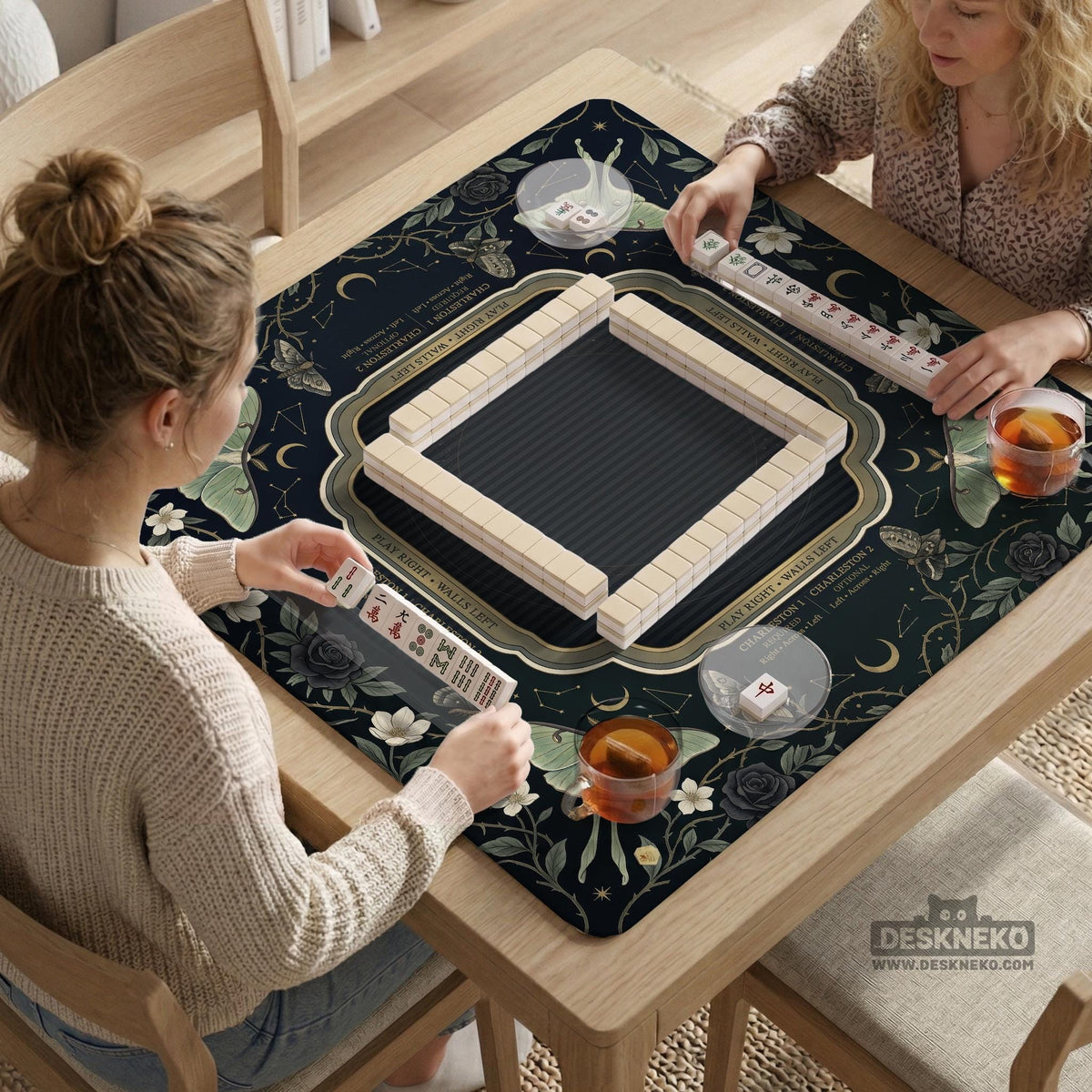 A dark floral mahjong mat with a scalloped edge, moth and flower artwork, and an American Mahjong rules layout on a dark background.